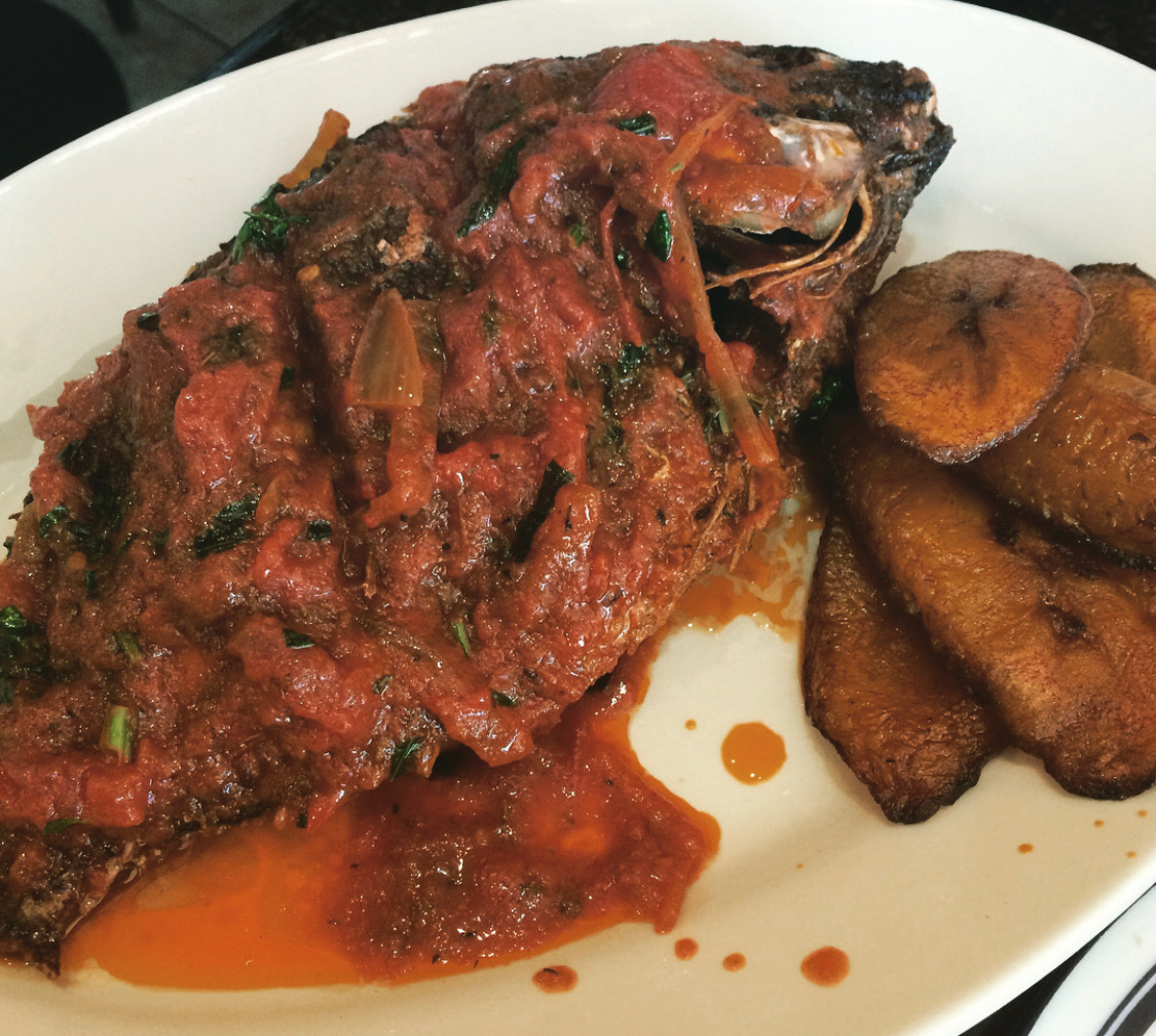 An image of a fish dish covered with sauce and plantains on the side.