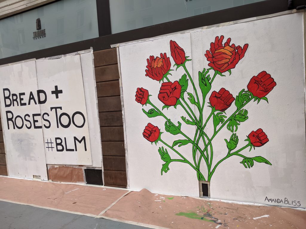 A mural with a white background says "bread and roses too BLM" with an image of roses adjacent to it.
