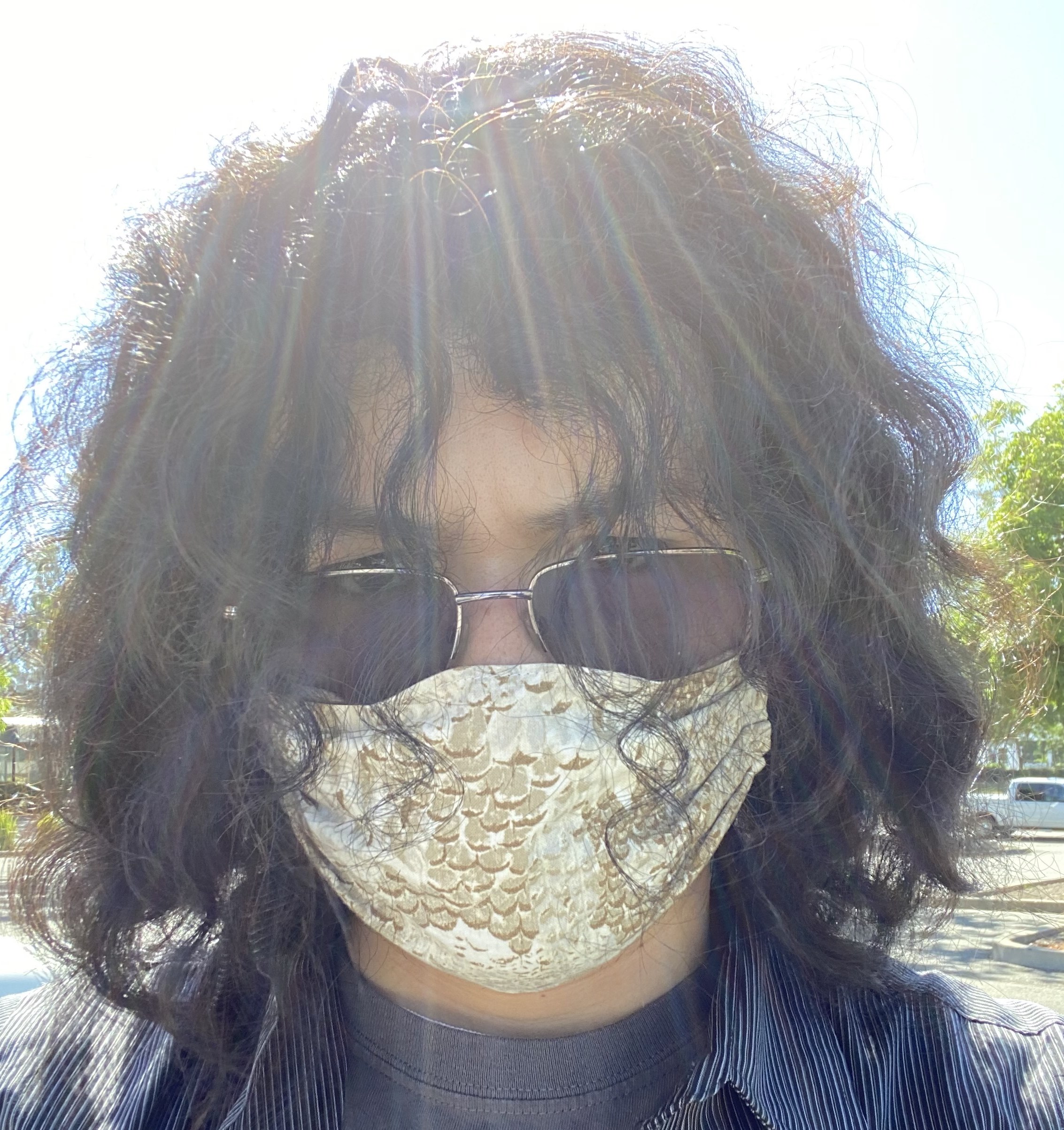 A young man wearing a mask and sunglasses with long curly hair.