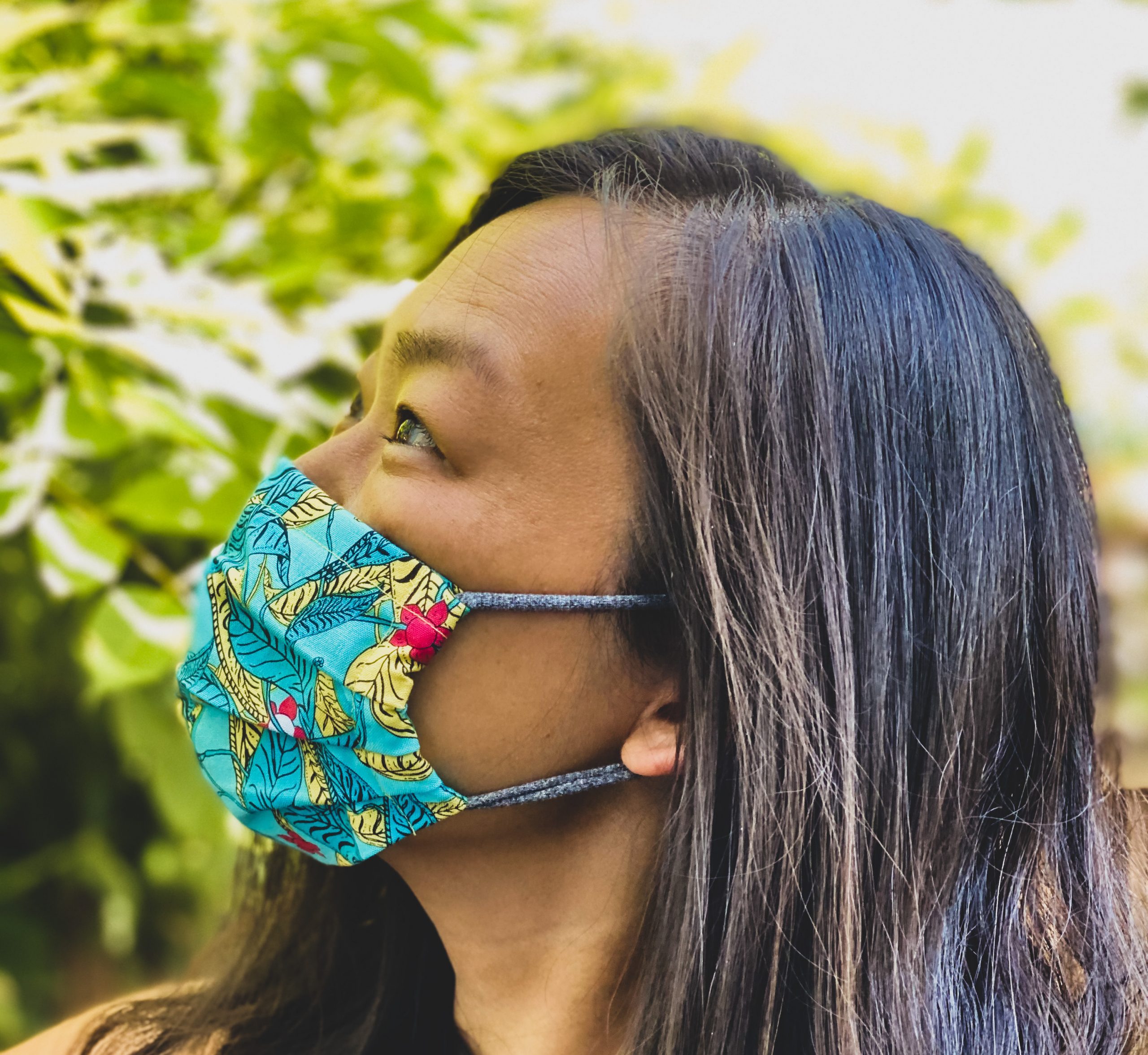 An Asian American woman poses for a profile photo wearing a colorful green mask.