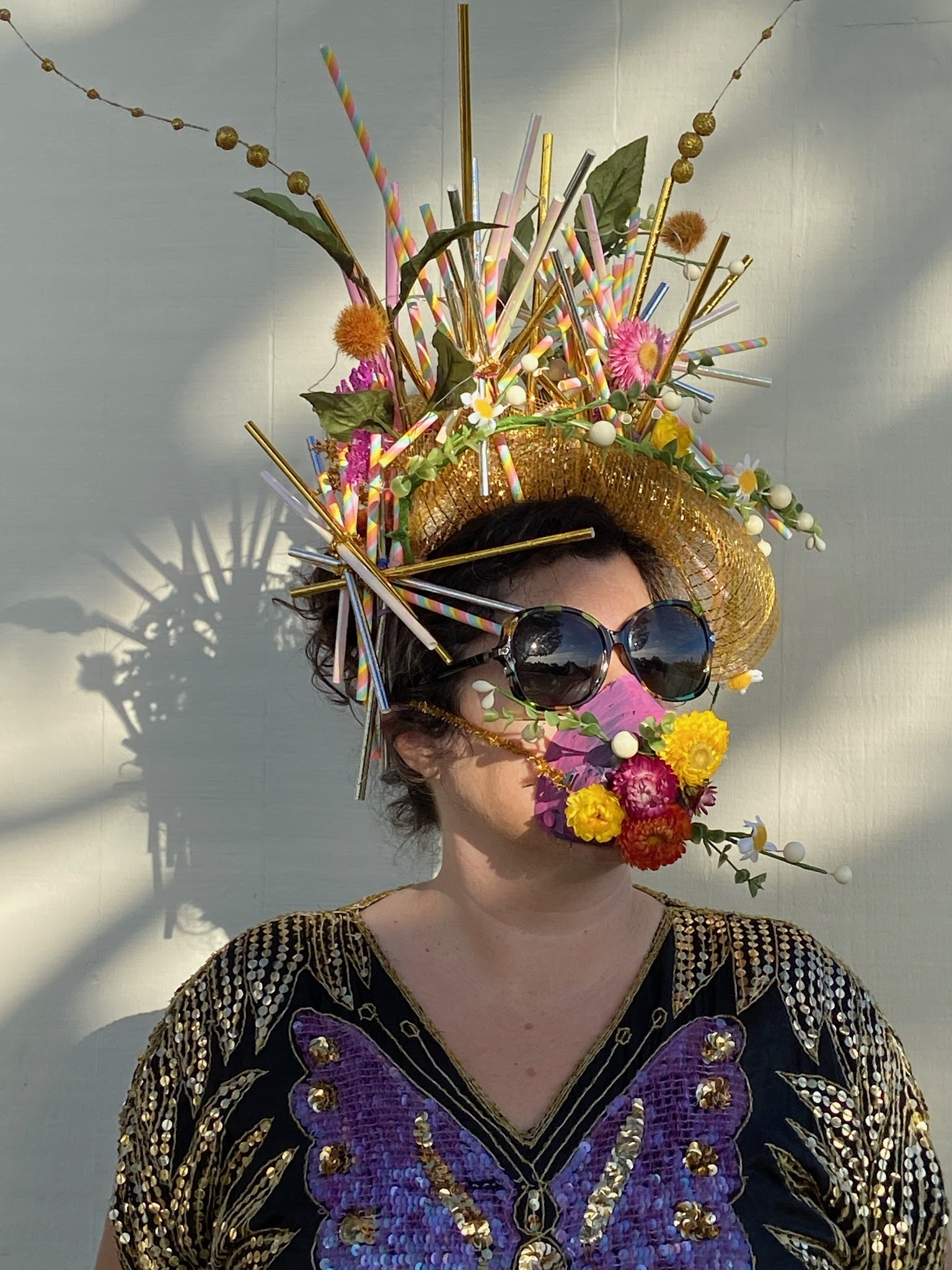 A woman wears a handmade crown made from flowers, and a mask that matches.