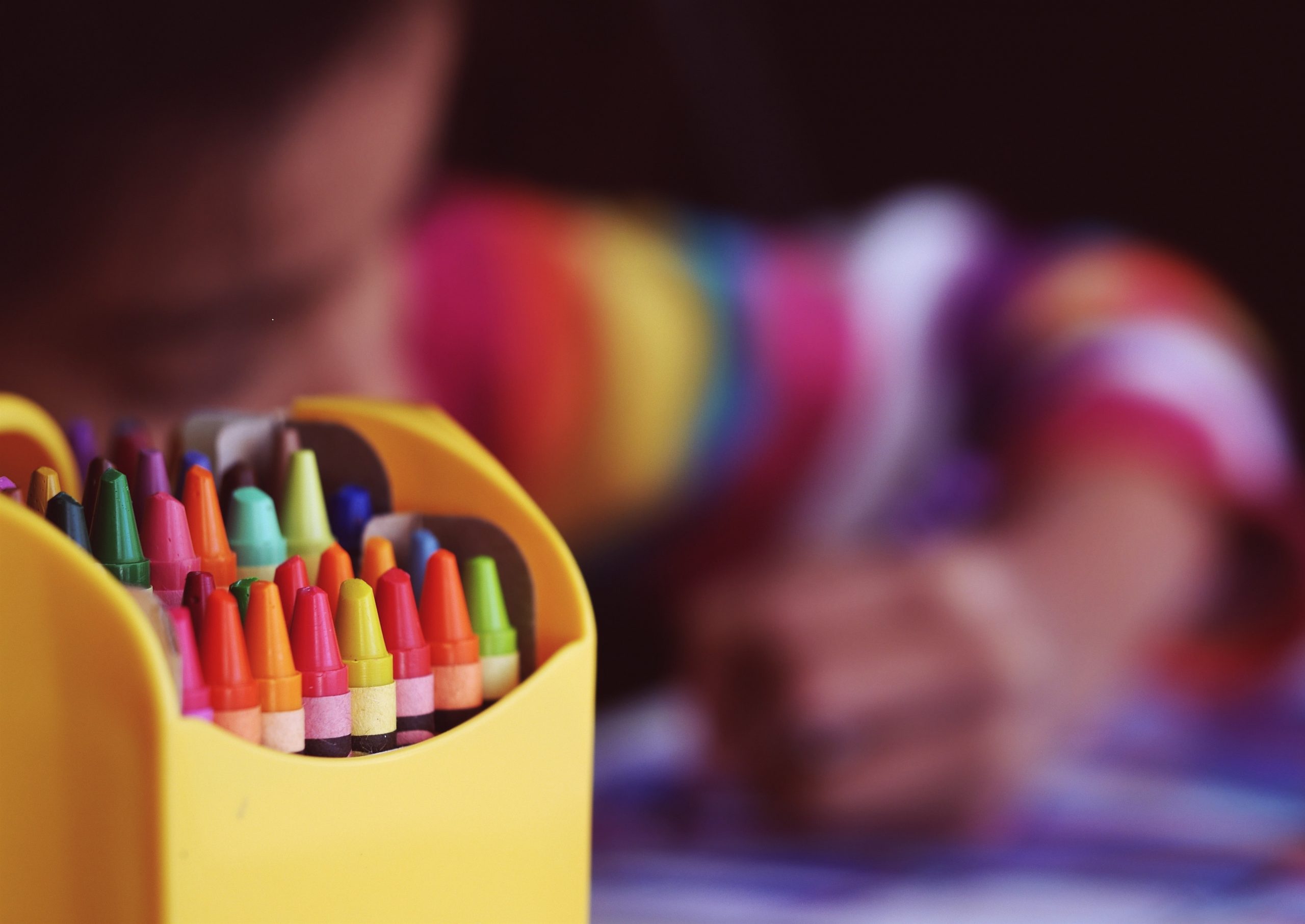A closeup of crayons and a child in the background coloring.