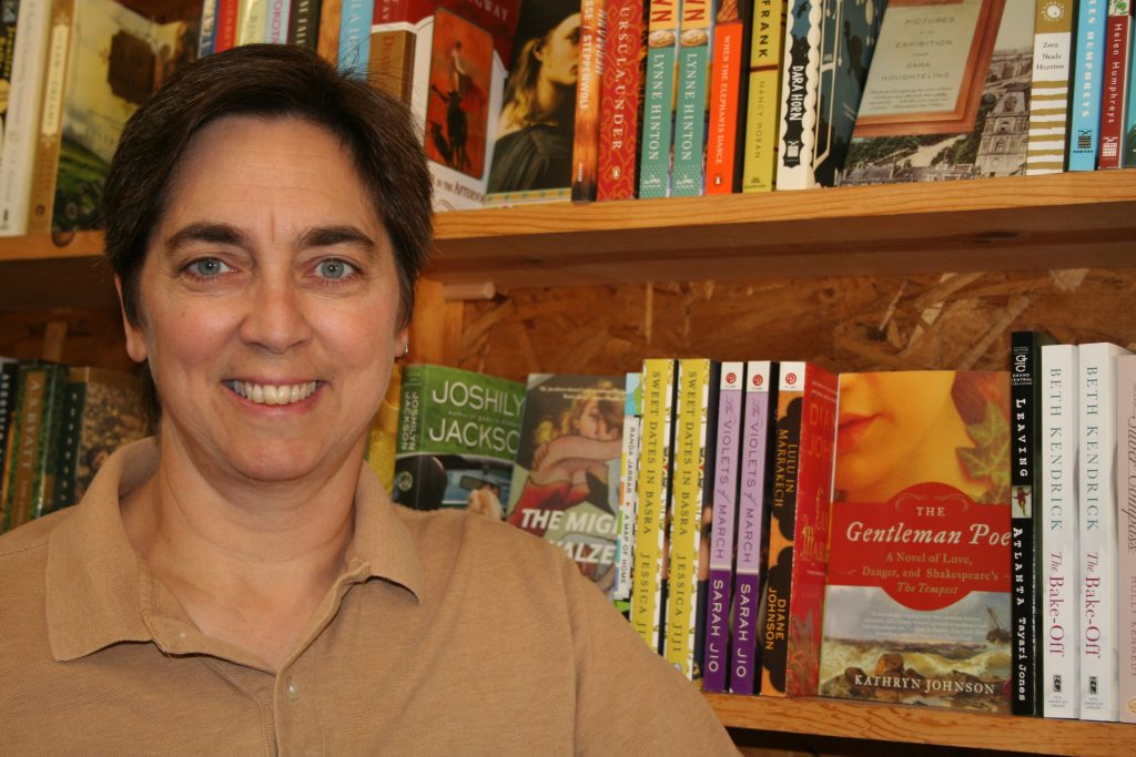 A woman with short brown hair stands in front of a shelf of books.