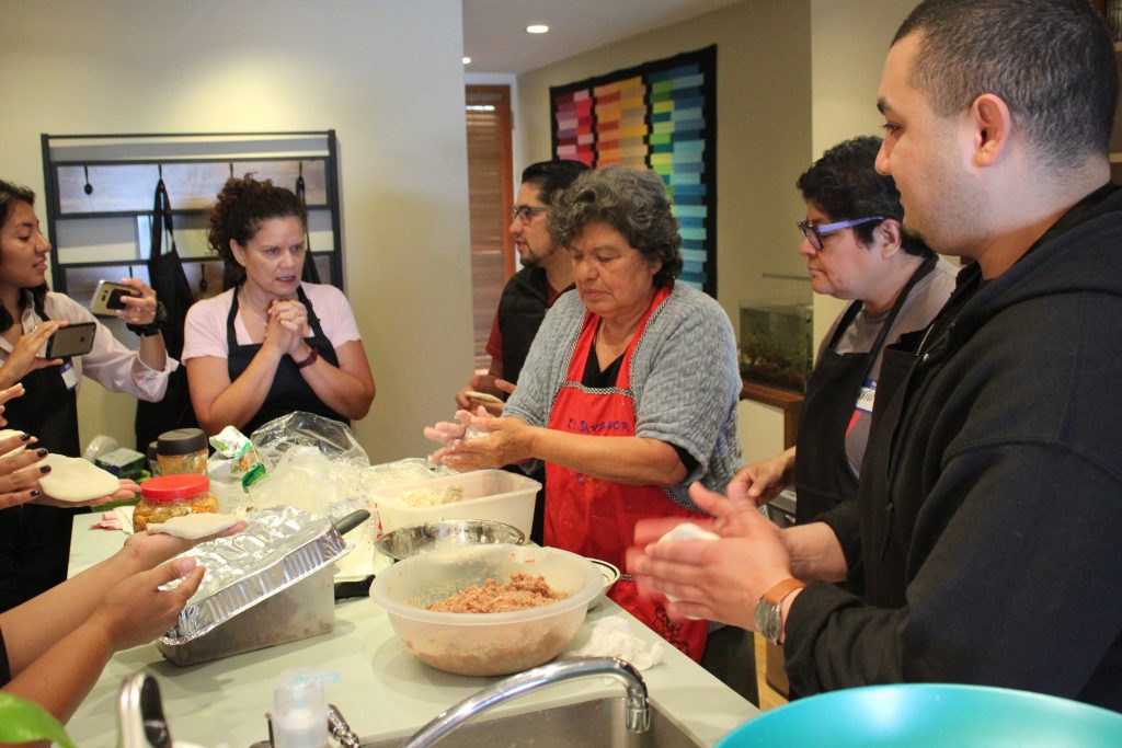 An image of several people gathered around a kitchen counter making pupusas by hand.