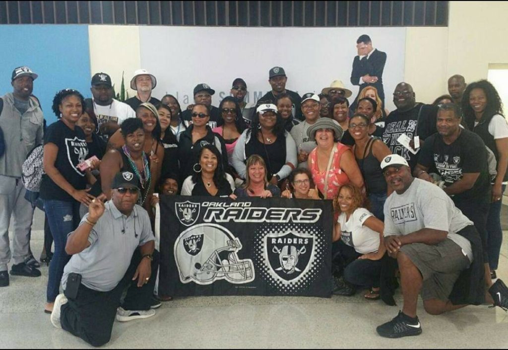 A large group of mostly African Americans pose with a Oakland Raiders banner