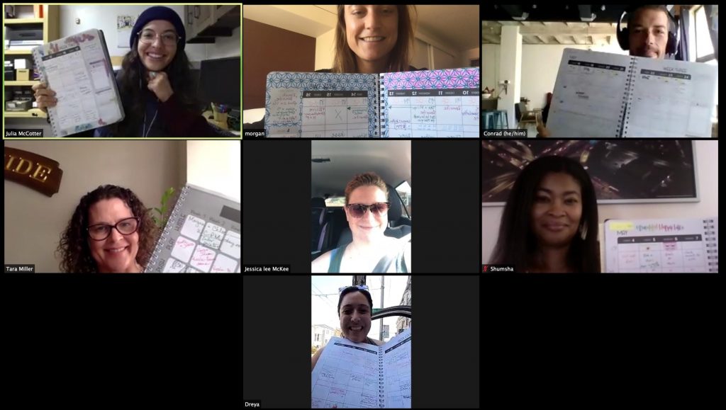 A screenshot of a diverse group of people holding up a planner/workbook during a Zoom.