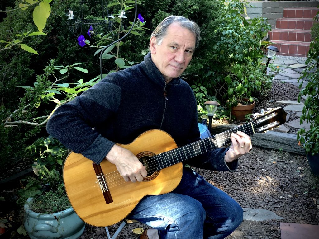 An image of a man with grey hair holding a guitar.