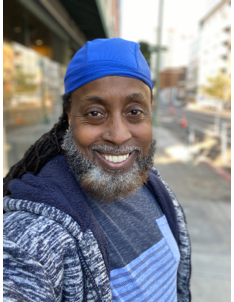 An African American man with a grey beard takes a selfie.