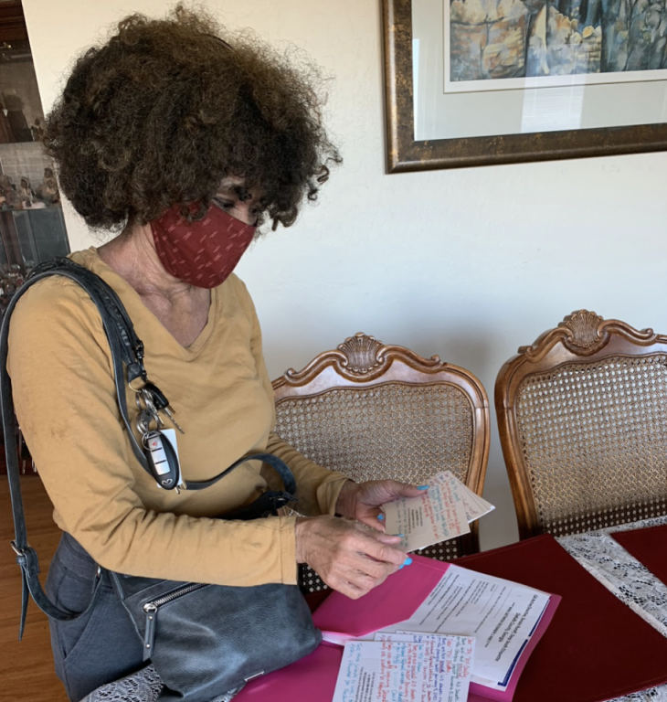 An African American woman wearing a face mask checks postcards.