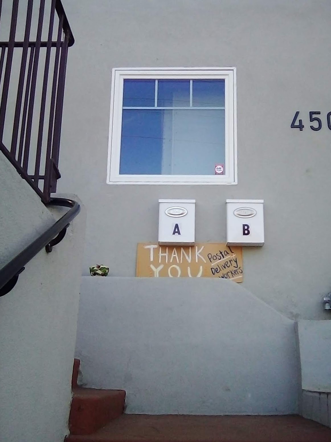 a grey stone house with a handwritten cardboard sign thanking postal workers