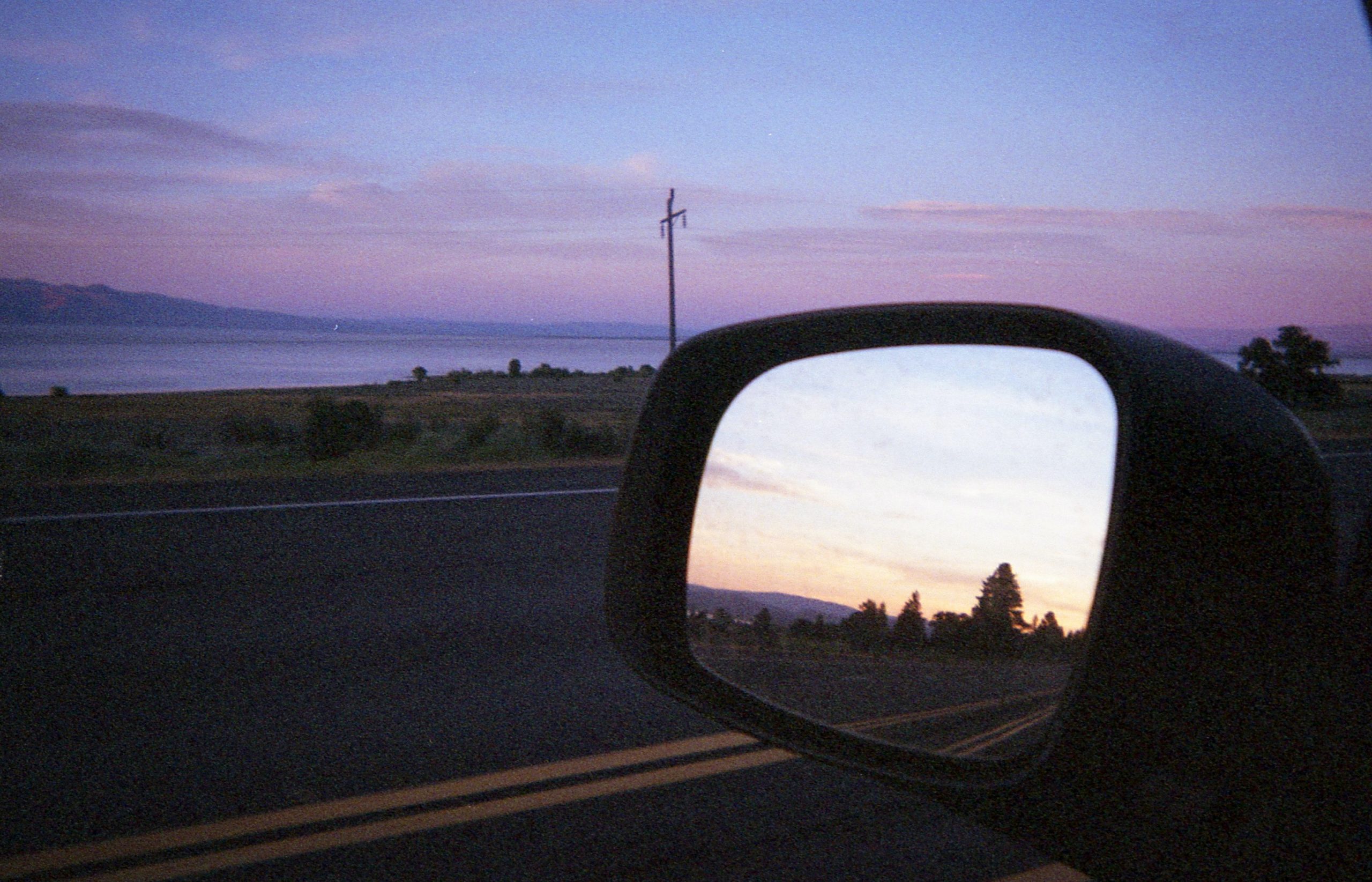 An image at dusk of a rearview mirror and pretty pink clouds.