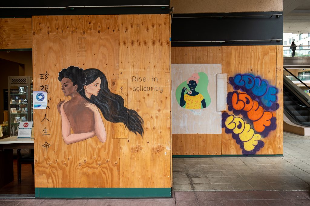 An image of a young Asian woman hugging a Black woman painted on wooden boards.