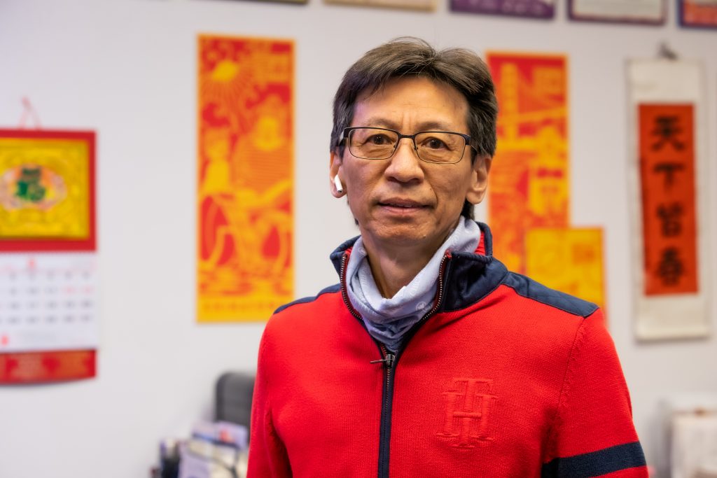 A Chinese American man stands in an office with bright new year banners in the back.