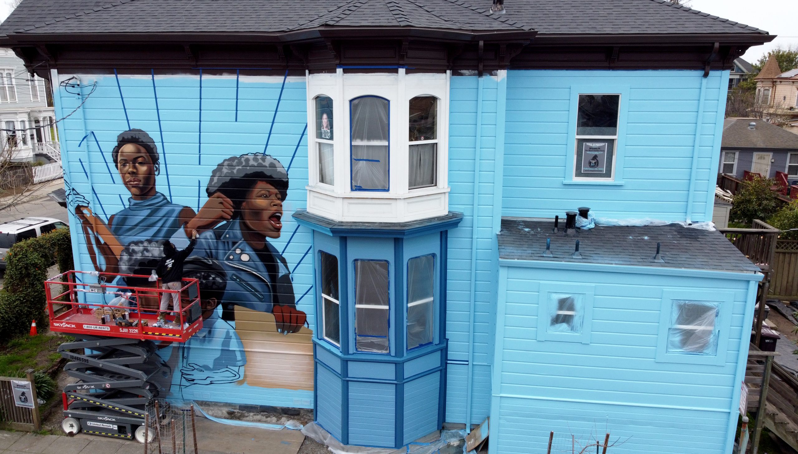 An image of a Victorian home painted with baby blue and images of powerful Black women from the Black Panther Party painted on the outside of the house in West Oakland.