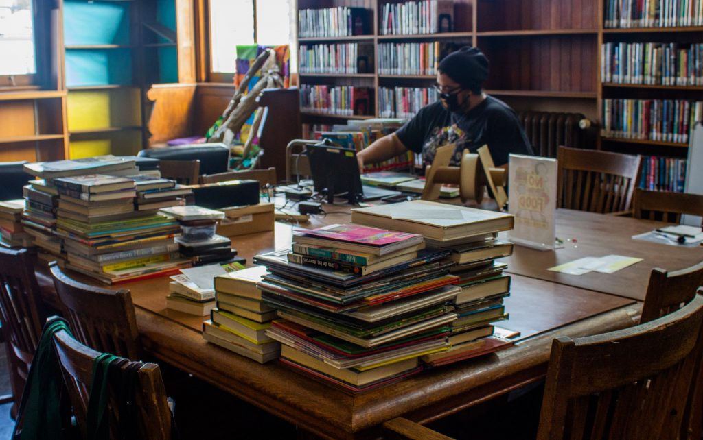A librarian behind a desk piled high with books