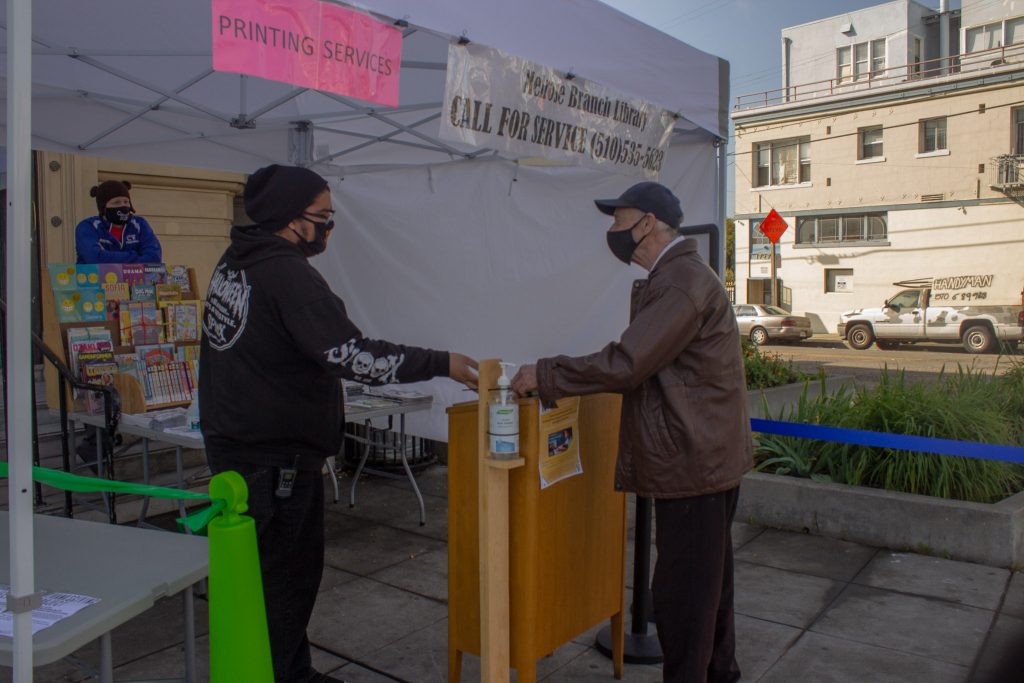 A librarian gives out books to an elder wearing masks under a white tent