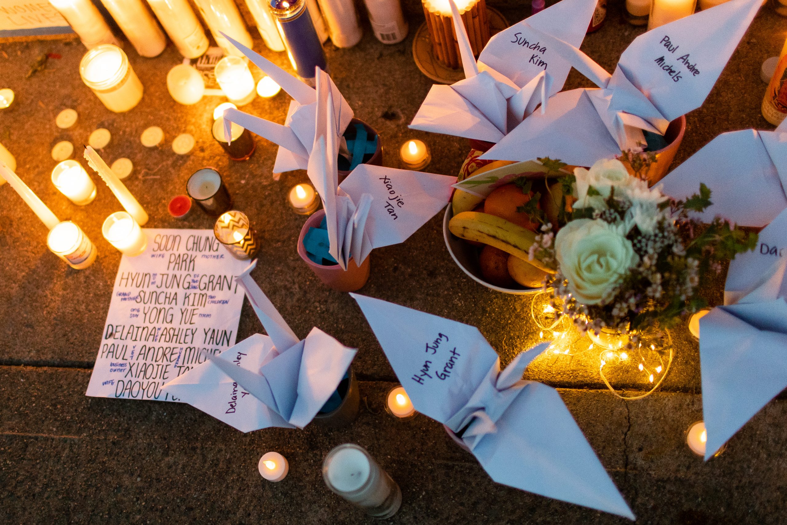 image of white paper cranes with names of Atlanta shooting victims and candles surround the cranes