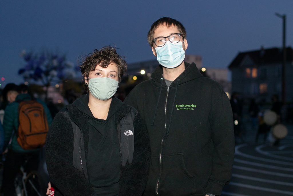 A white woman and white man wearing surgical masks pose for photo in the evening at Madison Park in Oakland.
