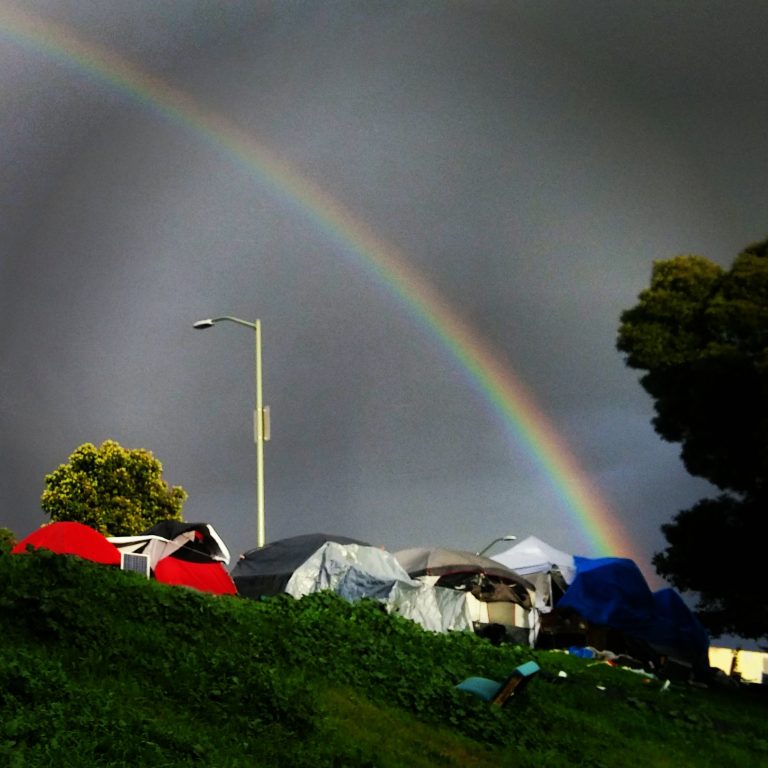a rainbow over a homeless tent encampment in Oakland