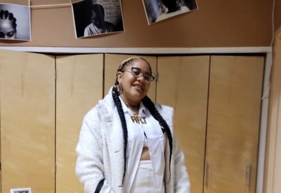 An African American woman with braids and glasses smiles for camera inside an art building 