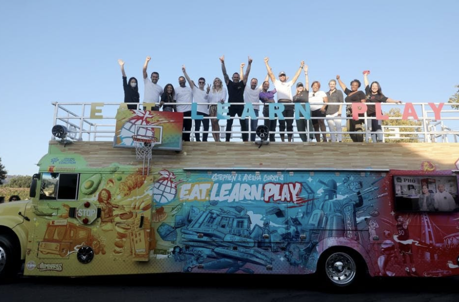 People stand on top of a colorful bus with their hands raised.