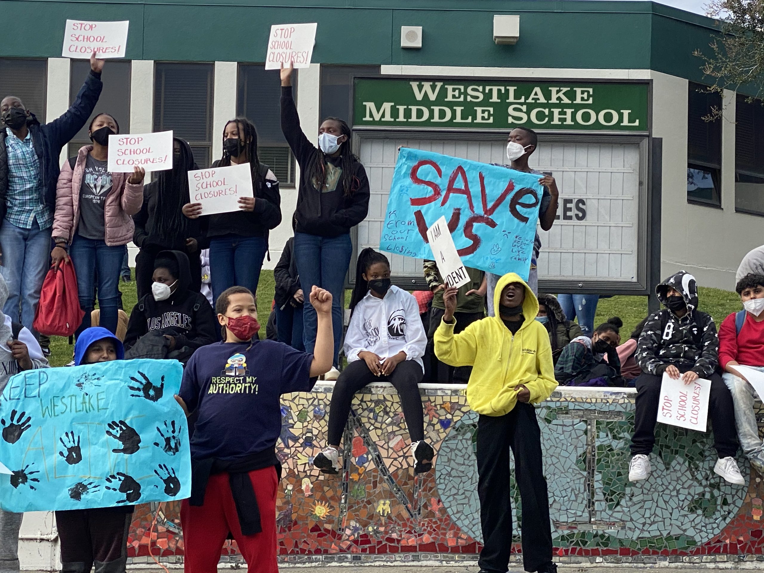 students holding signs outside middle school saying "save us"