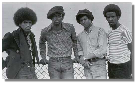 a black and white photo of four young African American men looking stylish and serious in hats