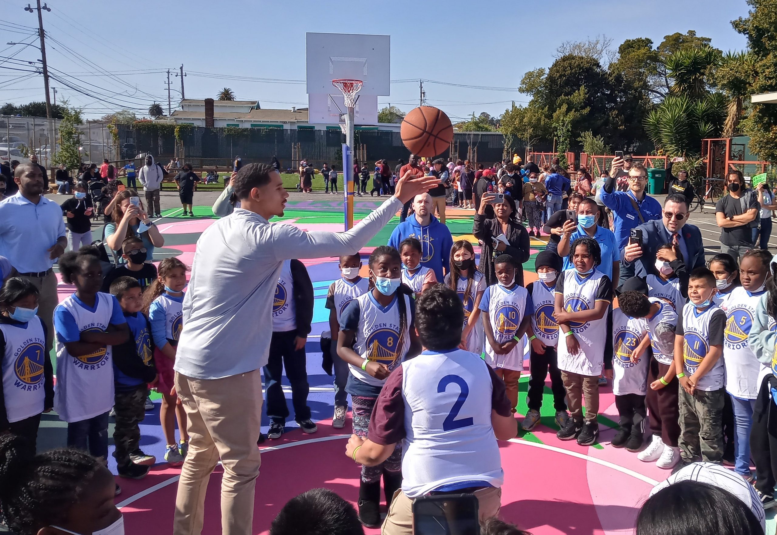 image of tall NBA player with mustache in new basketball court at elementary school, with a bunch of elementary kids surrounding him