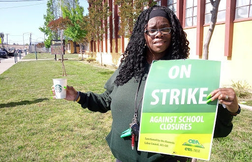 An African American woman holds a sign that says ON STRIKE