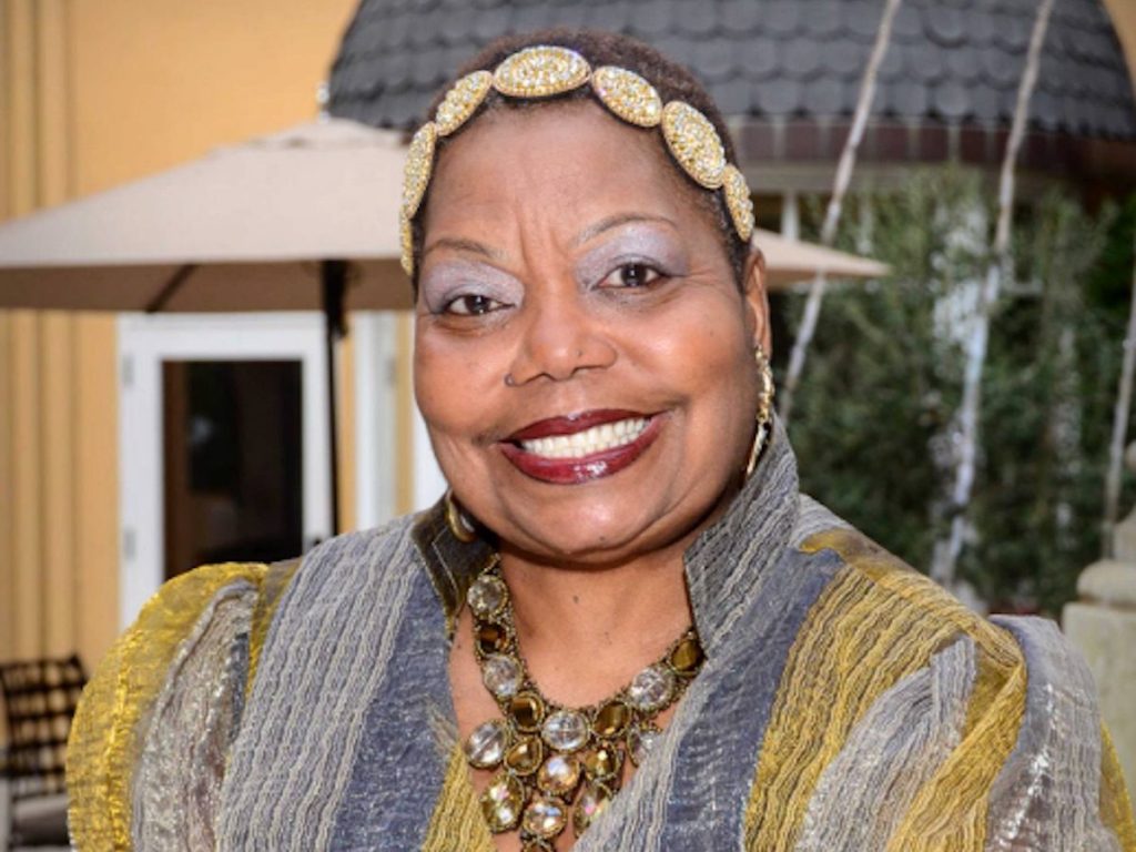 An African American woman wearing a gold headband smiles for camera