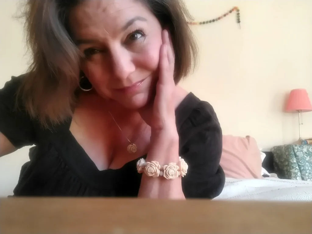 A woman with brown hair and rose bracelet looks into camera for a selfie