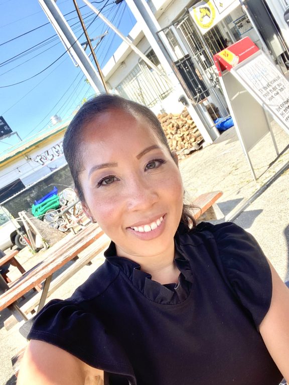 Asian American woman wearing black dress and ponytail smiles for camera