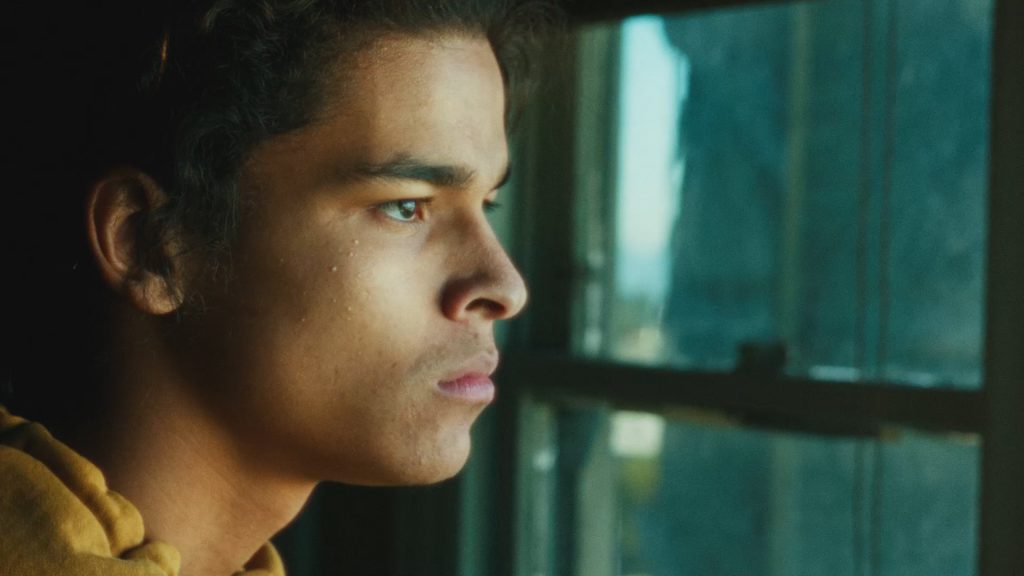 An Indigenous young man stairs off to the right of screen, looking angry and contemplative