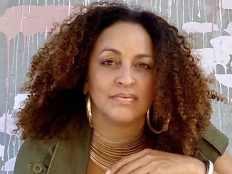 A mixed race African American woman with curly brown hair wears olive green shirt and poses for photo