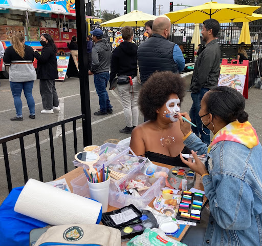 a Black face painter paints a Black woman's face at a festival