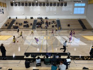 A new shiny basketball court inside a high school, with players scrimmaging