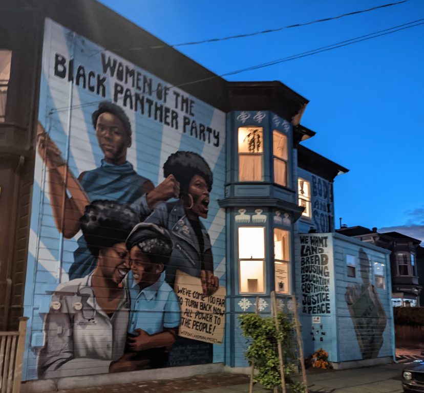 A large blue mural of Black women painted on a tall Victorian era home.