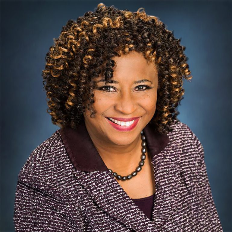 And African American woman with curly hair wearing a wool blazer smiles for portrait
