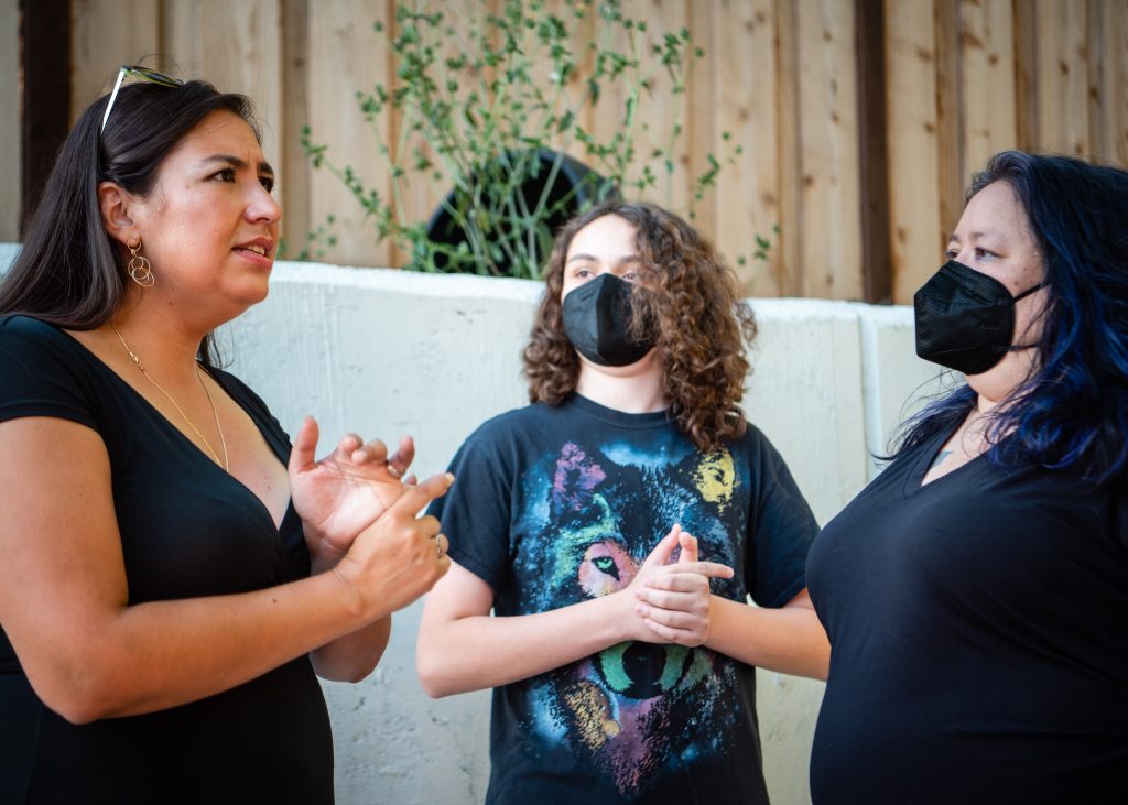 A woman with dark brown hair talks with two people who are wearing masks