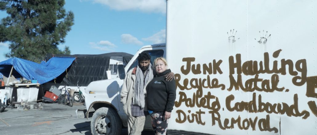 two people stand in front of a white truck that has hand lettering on it saying "junk hauling, metal..."