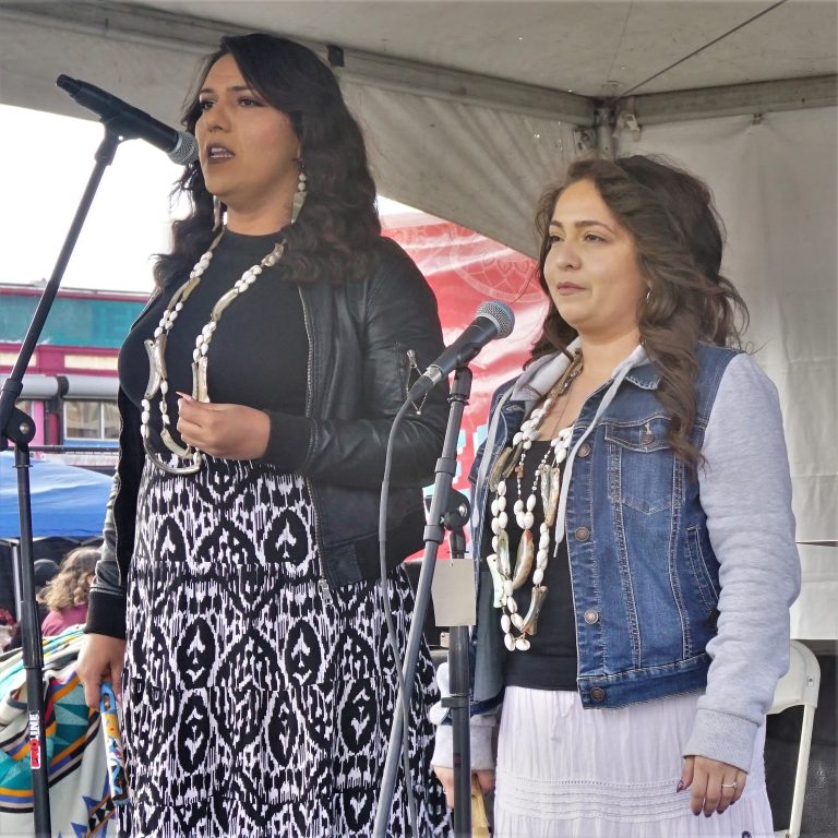 Two Ohlone women sing on a stage