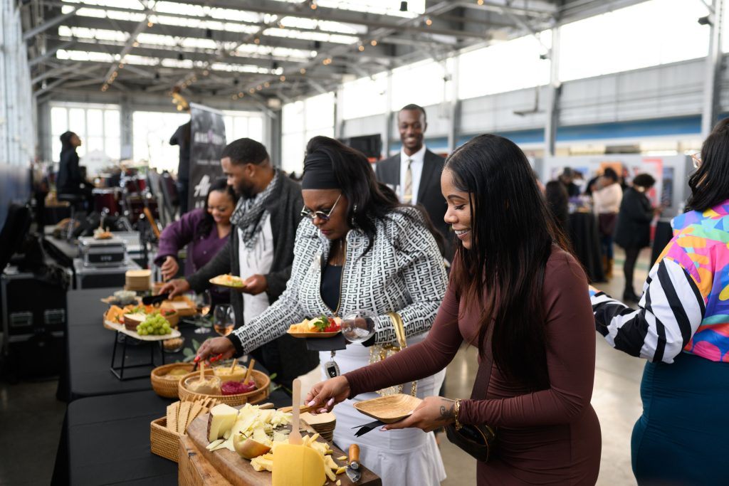 A group of mostly African Americans dressed formally enjoy wine and food at a festival at various tables