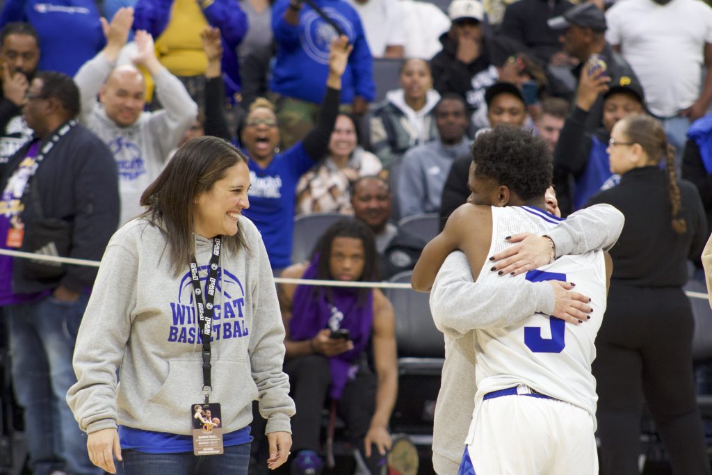 An African American boy basketball players hugs an Asian American woman coach while another woman smiles at them
