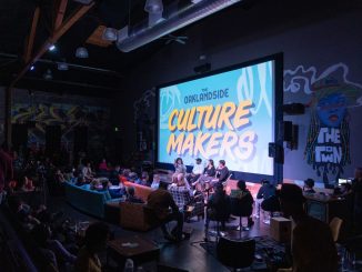 a dark theater with a screen that says "Oaklandside Culture Makers" and a panel in front