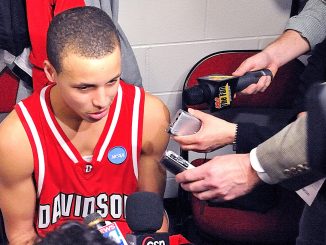 A young mixed race basketball player wearing a red jersey speaks into a mic after a game