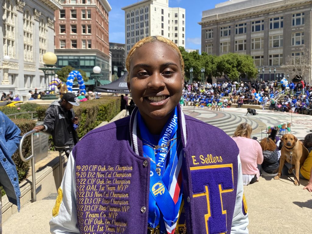 An African American girl wearing a purple letterman's jacket smiles for camera