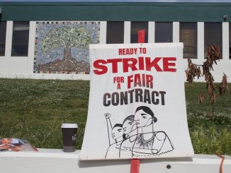 A canvas sign on a stick that says "strike for a fair contract"