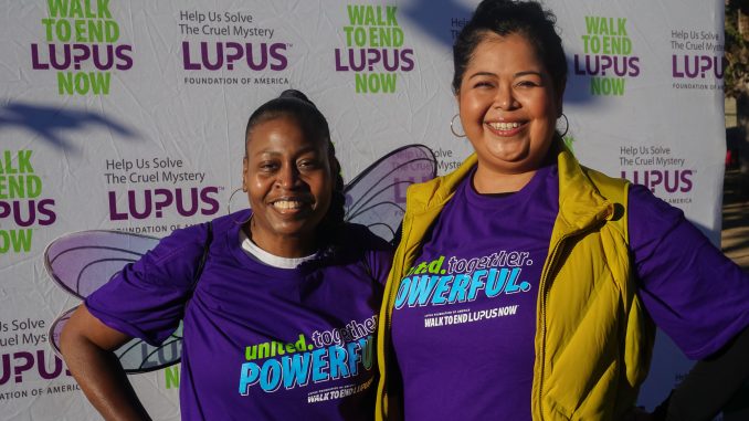 An African American woman and Latina woman stand next to each other during a charity walk wearing purple t-shirts