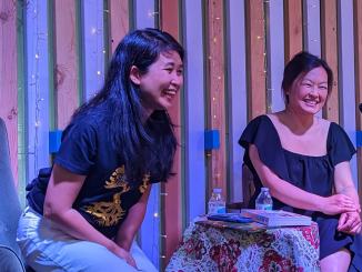 two asian american women sit on a stage and smile