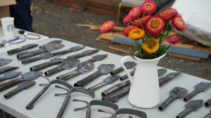 a table with gardening tools, along with a vase of red and orange flowers